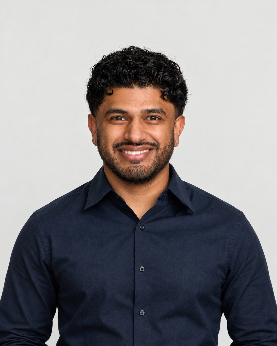 Harshith smiling in a navy shirt against a soft stone gray background